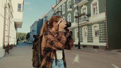 Young Caucasian woman captures urban scenes with camera on sunny city street. Serene mood enhances her focused expression.