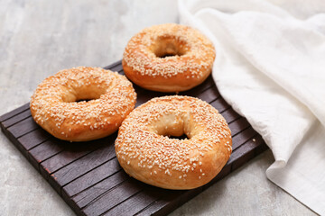 Wooden board of tasty bagels with sesame seeds on grey background, closeup