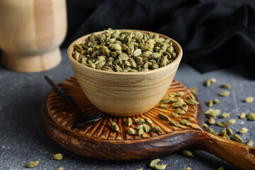Wooden bowl with cardamom spice on grey background
