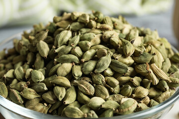 Glass bowl with cardamom spice on grey background, closeup