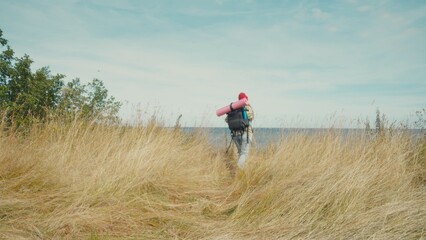 Contemplative woman walks along serene seashore carrying backpack and exercise mat. Natural environment evokes peace and tranquility.