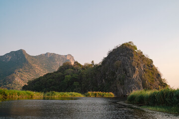 Fototapeta premium The mountain looms over a green landscape where a swamp meets a tranquil lake, water reflecting the sky, a single cloud drifting in peaceful, untouched nature.