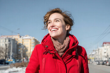 joyful woman steps outside in bright red coat smiling widely under clear blue sky