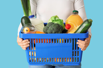 Woman holding shopping basket with different fresh products on blue background
