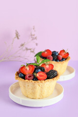 Sweet tartlets with different fresh berries and mint on lilac background