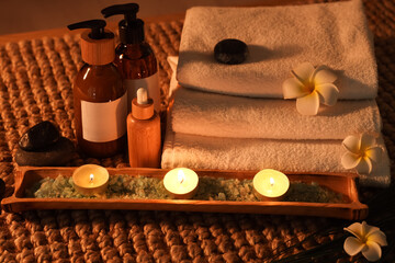 Beautiful composition with towels, cosmetic products, sea salt, candles and spa stones on wicker table in dark salon