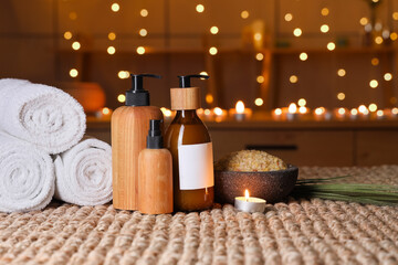 Beautiful spa composition with towels, cosmetic products, candle and sea salt on wicker table in dark salon