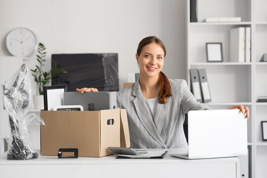 Young happy businesswoman with laptop and cardboard box of belongings in office on moving day