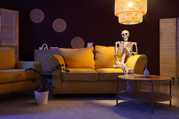 Human skeleton model sitting on yellow sofa in living room at night
