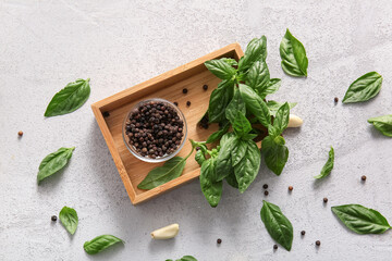 Wooden box with fresh green basil leaves, peppercorns and garlic on grey background