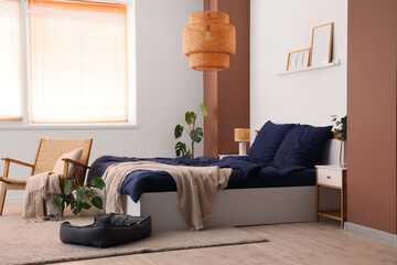 Stylish blue bedding, armchair, bedside tables, pet bed, hanging lamp and houseplants in bedroom