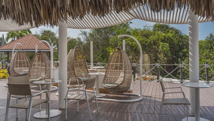 The recreation area at the resort. Wicker swings, tables, chairs on the outdoor terrace. Rope railings, latticed and thatched awnings. Green tropical vegetation. Cuba. Varadero.