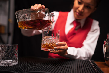Bartender woman pours whiskey into a glass in a restaurant.	
