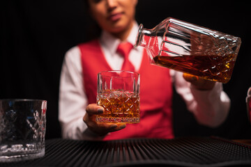 Bartender woman pours whiskey into a glass in a restaurant.	