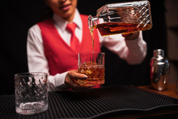  Bartender woman pours whiskey into a glass in a restaurant.