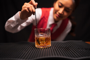  Bartender woman pours whiskey into a glass in a restaurant.
