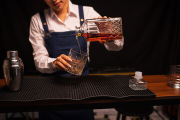  Bartender woman pours whiskey into a glass in a restaurant.