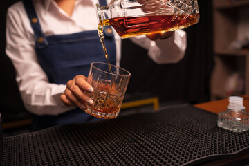 Bartender woman pours whiskey into a glass in a restaurant.	
