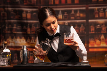  Bartender woman pours whiskey into a glass in a restaurant.