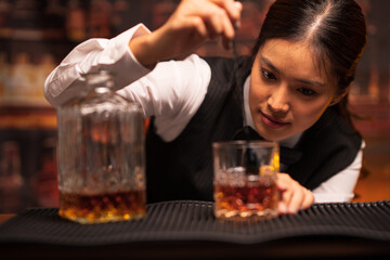  Bartender woman pours whiskey into a glass in a restaurant.