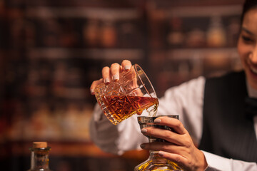  Bartender woman pours whiskey into a glass in a restaurant.
