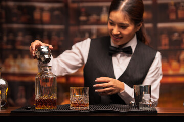 Bartender woman pours whiskey into a glass in a restaurant.	

