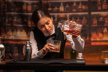 Bartender woman pours whiskey into a glass in a restaurant.	