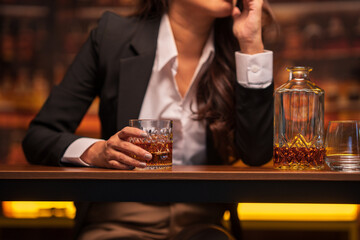 Asian woman in a black suit sitting holding a glass of whiskey at night in a restaurant.