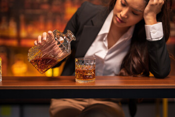 Asian woman in a black suit sitting holding a glass of whiskey at night in a restaurant.