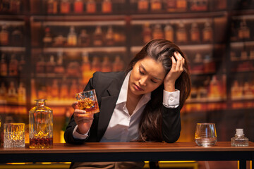 Asian woman in a black suit sitting holding a glass of whiskey at night in a restaurant.