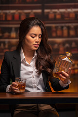 Asian woman in a black suit sitting holding a glass of whiskey at night in a restaurant.