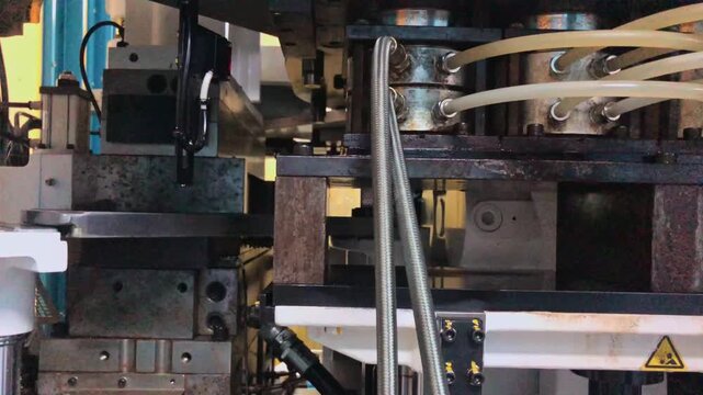 Blow molding machine producing clear plastic bottles on factory production line.