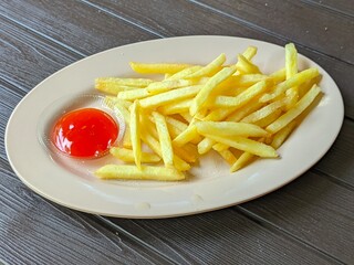 This image shows a plate of French fries served with chili sauce. The fries are golden yellow, thin, and crispy, neatly placed on a beige oval plate