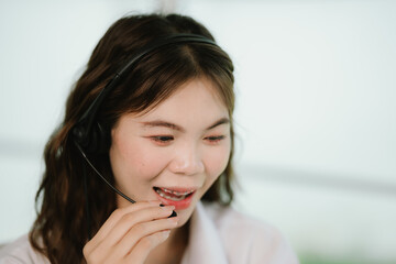 A young woman wearing a headset works at a desk in a call center, smiling as she provides customer support and online assistance.