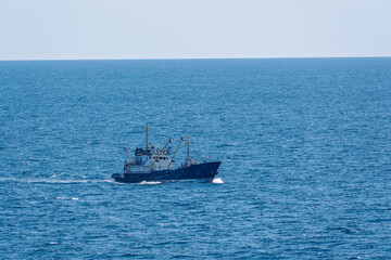 Fishing boat in blue sea and clear sky with birds flying overhead.