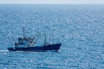 Fishing boat in blue sea and clear sky with birds flying overhead.
