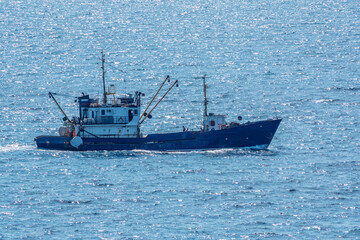 Fishing boat in blue sea and clear sky with birds flying overhead.