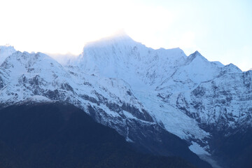 Fototapeta premium Jagged, snowy peaks loom under a cloudy sky Yala Snow Mountain, Sichuan, China