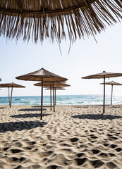 Fototapeta premium Straw Umbrellas on a Sunny Beach with Clear Blue Sea
