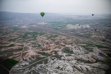 A panoramic view from a hot air balloon over Cappadocia. From a bird's-eye view, a unique landscape unfolds, featuring whimsical volcanic rock formations, winding roads, and patches of green fields.