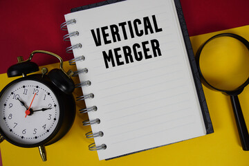 Vertical Merger text written on notebook paper with magnifying glass and alarm clock