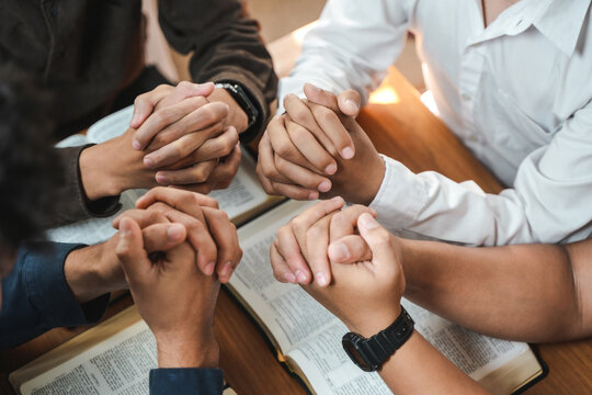 A group of Christians pray together over a wooden table for worship and the Bible.