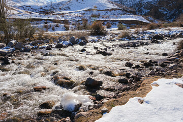 Mountain river flowing through a snowy landscape. Scenic water stream with rocks and snow-covered hills in winter. Natural environment.