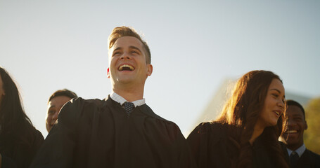 Smile, man and students and graduation outdoor for education, celebration and class success. Below, people and waiting for diploma of college achievement, award announcement and certificate ceremony