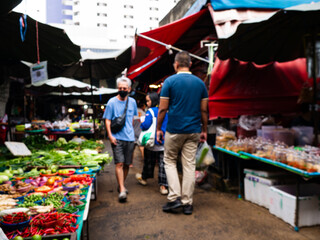 Obraz premium Blurred View of Shoppers at Local Market with Fresh Vegetables Stall.