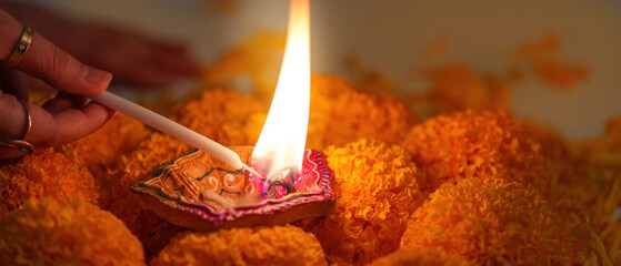 Diwali Festival. Lighting a traditional diya surrounded by marigold flowers.