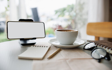 smart phone on stand with coffee cup, note book and diary on table