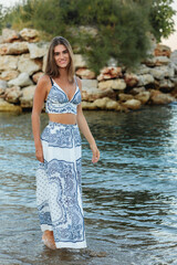 Young woman in stylish summer outfit by the water  at sea on the beach