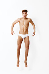 Fototapeta premium Surprised young man jumping with excitement, showcasing toned physique. White background emphasizing his expression and movement. Fitness and emotion concept.