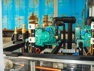 Industrial refrigeration system with green compressors, black pipes, and blue accents.